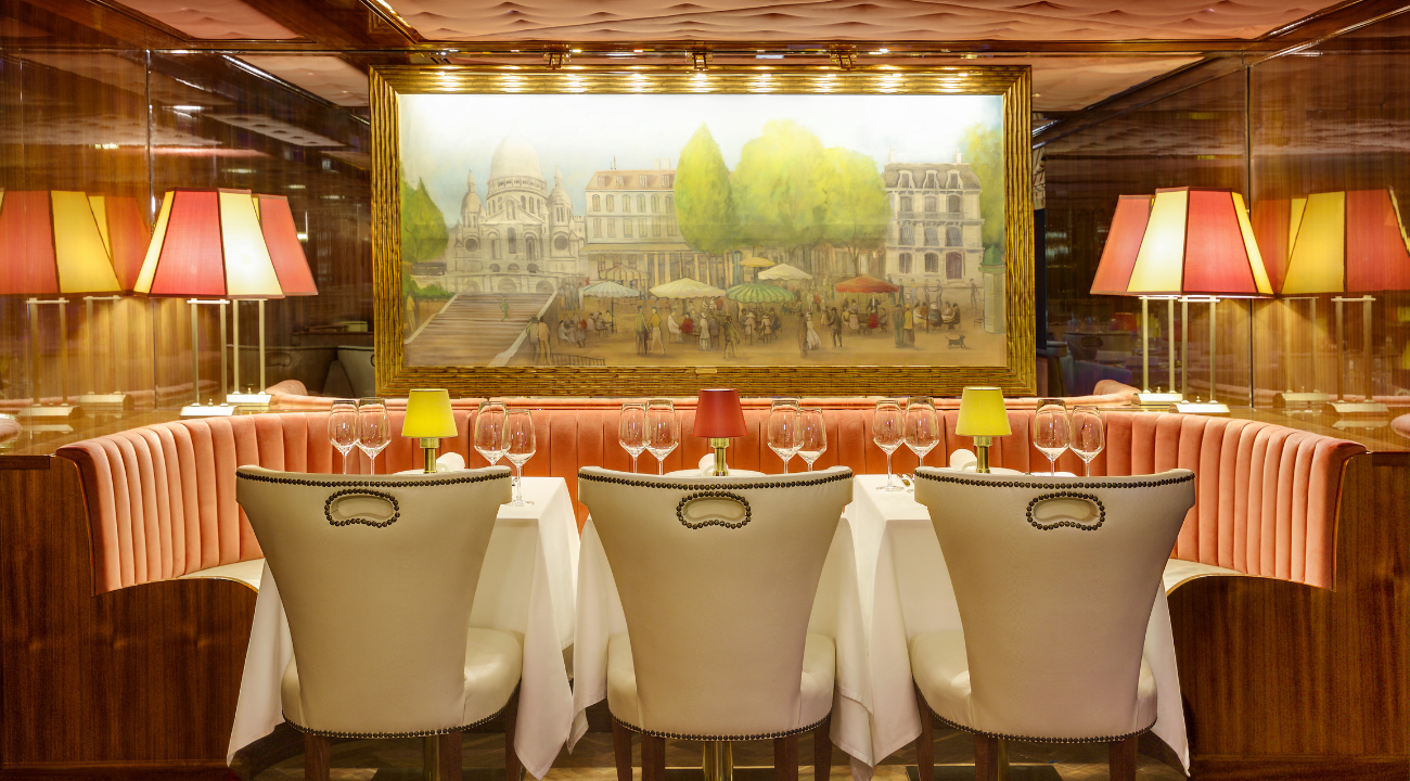 A beautifully set dining table onboard the S.S. Joie de Vivre featuring original Parisian-style artwork. Where you will dine every night of the Paris and Normandy river cruise.
