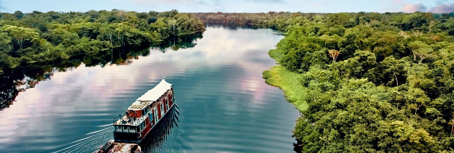 An aerial view of a river ship navigating the winding waterways of the Peruvian Amazon surrounded by dense tropical jungle.